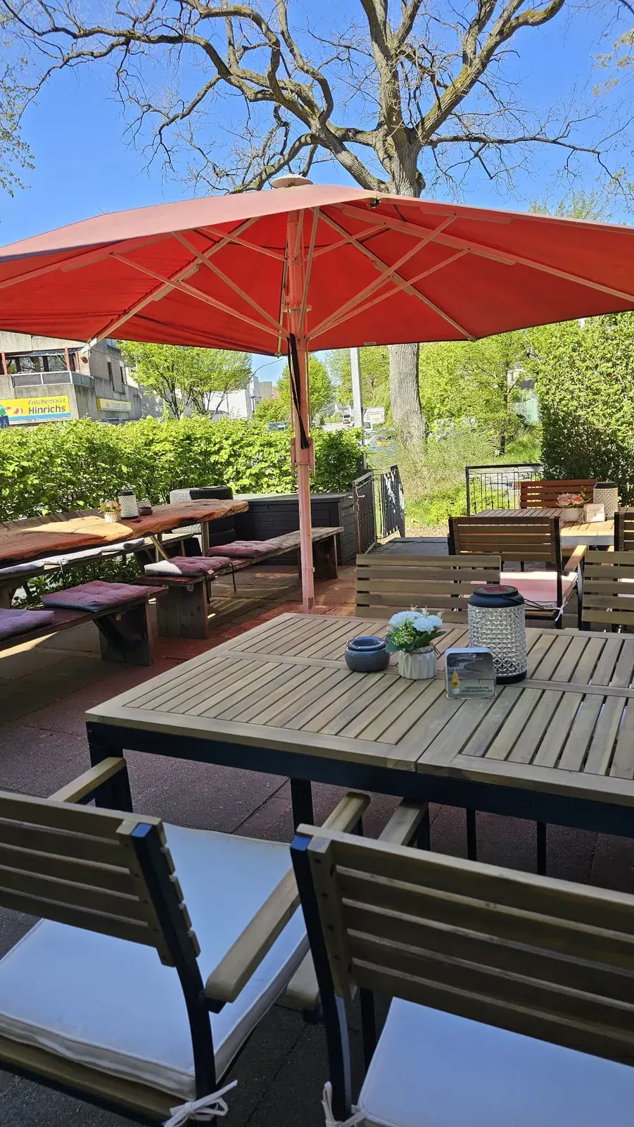 Die Terrasse mit Holztischen, roten Sonnenschirmen und Bierbänken